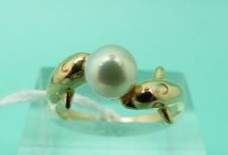 An 18ct gold ring in the form of two dolphins set with a pearl between (Size M)