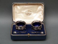 A cased pair of hallmarked silver open salts with blue glass liners,