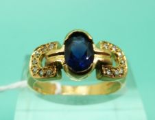 A yellow metal ring set with oval cut sapphire and diamonds in a stylised buckle design (Size M)