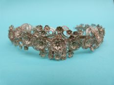 A white metal filigree headband/tiara decorated with tiered flowers and leaves