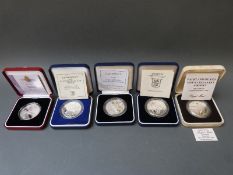 Four cased and certificated Alderney crowns together with a Falkland Island Mount Pleasant Airport