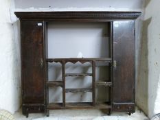 An antique oak wall unit having various shelves flanked by cupboards and drawers with dentil frieze