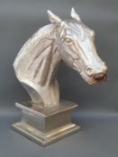 A cast metal bust of a horse's head on similar metal plinth,