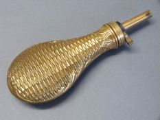 An all brass powder flask with embossed geometric decoration to both sides and acanthus leaf border,