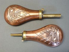A pair of copper and brass powder flasks both with embossed decoration of a cannon,