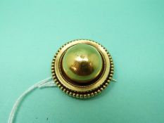 A Victorian yellow metal brooch with a half sphere to the centre surrounded by rope twist border