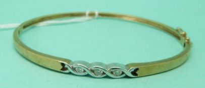 A 9ct gold bangle set with three diamonds in a white gold setting