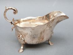A George V hallmarked silver sauce or gravy boat with scroll handle raised on three feet,