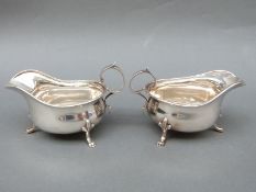 A pair of George V hallmarked silver gravy or sauce boats, raised on three feet with scroll handle,