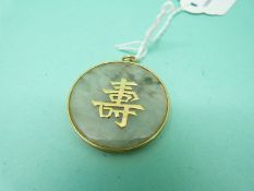 A Chinese yellow metal pendant set with a jadeite section and Chinese characters to the centre