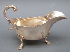 A Edward VII hallmarked silver sauce or gravy boat with scroll handle raised on three feet,