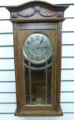 An oak-cased c1910 wall clock in lightly carved case with, bevelled glass door,