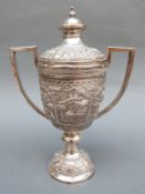 An Indian white metal pedestal lidded trophy cup with all round repousse decoration of buildings