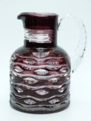 An amethyst flash overlaid glass water jug with cut decoration and applied handle,