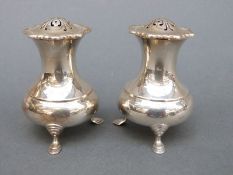 A pair of George V hallmarked silver peppers raised on three feet, Sheffield 1934,