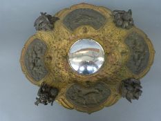 A gilt metal and bronze dish with four panels each depicting countryside scenes interspersed with