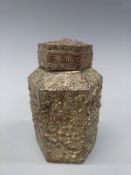 A Japanese embossed metal hexagonal tea caddy decorated with flowers in vases with a Greek key