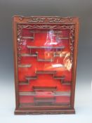 A Chinese carved and glazed display case carved with bats to the corners,