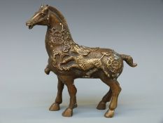A Japanese brass or bronze figure of a horse with relief decoration of mythical beasts,
