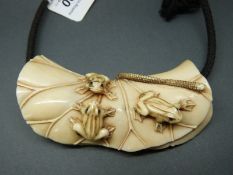 A Japanese Meiji period carved ivory pendant in the form of three frogs on a lotus leaf,