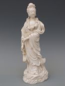 A Chinese blanc de chine figurine of Guanyin standing on a scrolling plinth,