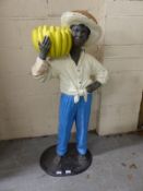 A shop display model of a young boy with hat and a bunch of bananas,