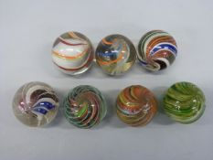 Seven large glass marbles, all with multicoloured latticino twists,