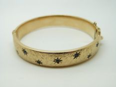 A 9ct gold bangle, the textured surface set with sapphires in star settings, 19.