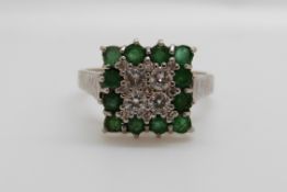 An 18ct gold white gold ring set with four diamonds surrounded by emeralds in a square setting