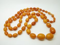 An amber necklace of 65 graduated ovoid egg yolk coloured beads, the largest approximately 22x18mm,
