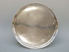 A George V hallmarked silver circular salver raised on hoofed feet,