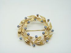 A 14k gold brooch set with cornflower blue sapphires in a foliate wreath design, 4.