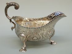 A Georgian hallmarked silver sauce boat with repousse decoration and scroll handle,