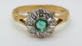 A 9ct gold ring set with a round emerald surrounded by diamonds in a flower cluster (size L)