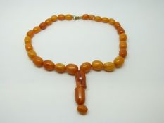 An amber prayer bead necklace of 28 graduated ovoid egg yolk coloured beads and two larger barrel