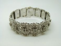 A white metal bracelet with raised floral decoration and each panel set with three cubic zirconia
