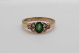 A 9ct gold ring set with an oval cut emerald and three diamonds to each shoulder (size O)