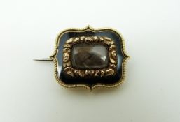 A Georgian mourning brooch set with plaited hair within foliate and black enamel border,