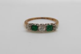 An 18ct gold ring set with three round cut diamonds and two square cut emeralds (size O)