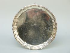 A George V hallmarked silver salver with shaped and reeded rim, raised on three paw feet,