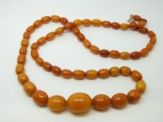 An amber necklace of 60 graduated ovoid egg yolk coloured beads, the largest approximately 20x15mm,