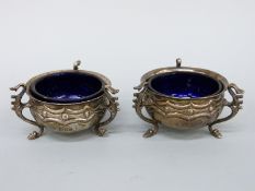 A pair of Edward VII hallmarked silver open salts with blue glass liners, on raised hoofed feet,