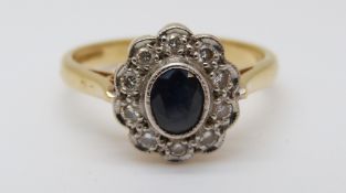 An 18ct gold ring set with a sapphire surrounded by diamonds in a cluster (size K)