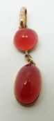 A yellow metal pendant set with a circular red cabochon and an oval red cabochon