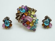 A silver brooch set with coloured paste in a stylised floral decoration and matching earrings