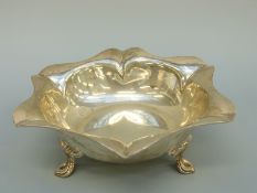 A George V hallmarked silver bowl with lobed crimped rim, raised on three teardrop shaped,