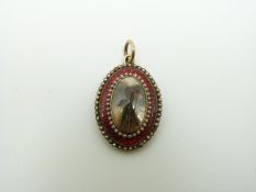 A Victorian pendant set with plaited hair to the centre surrounded by red guilloche enamel bordered