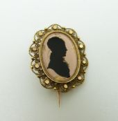 A 19thC yellow metal filigree brooch set with a reverse painted silhouette, 2.7 x 2.