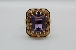 An 18ct gold ring set with an emerald cut amethyst with foliate border, 6.
