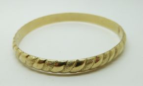 A 14k gold bangle with a textured surface,